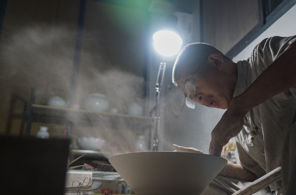 ↑ 在景德鎮(zhèn)，手工匠人吹去坯內(nèi)的泥土（2021年7月14日攝）。