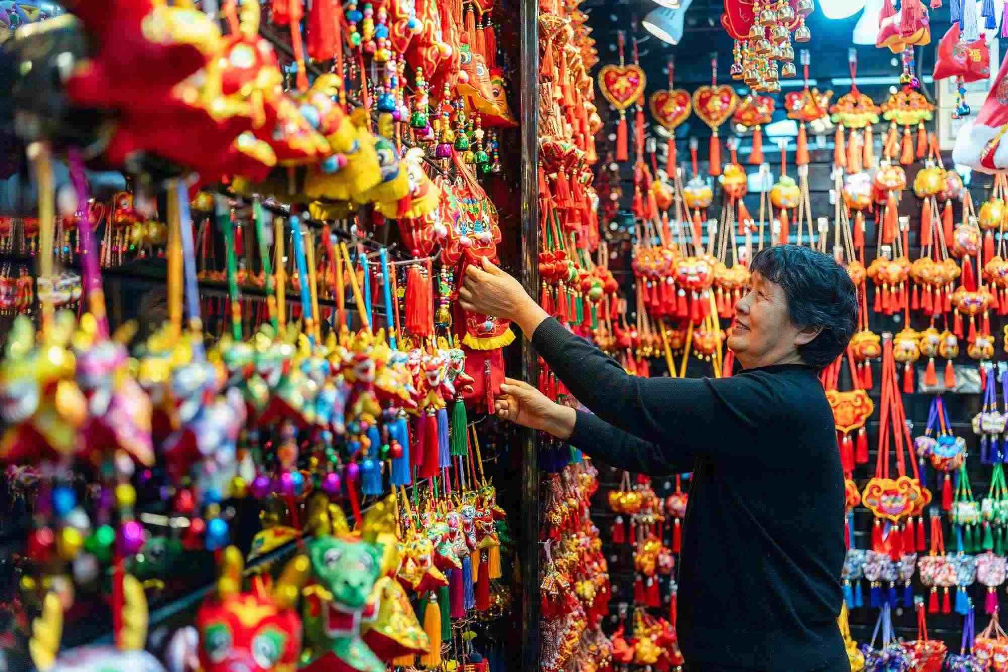 2023年12月11日，金華義烏國際商貿(mào)城，龍年喜慶用品掛滿攤位，顧客正在挑選中。