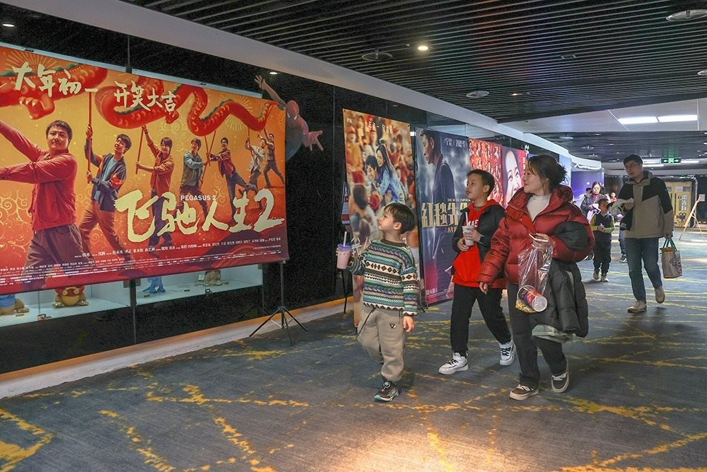 △ 2024年2月16日，在江西贛州一家電影院，觀眾從春節(jié)檔電影的宣傳展板前走過。