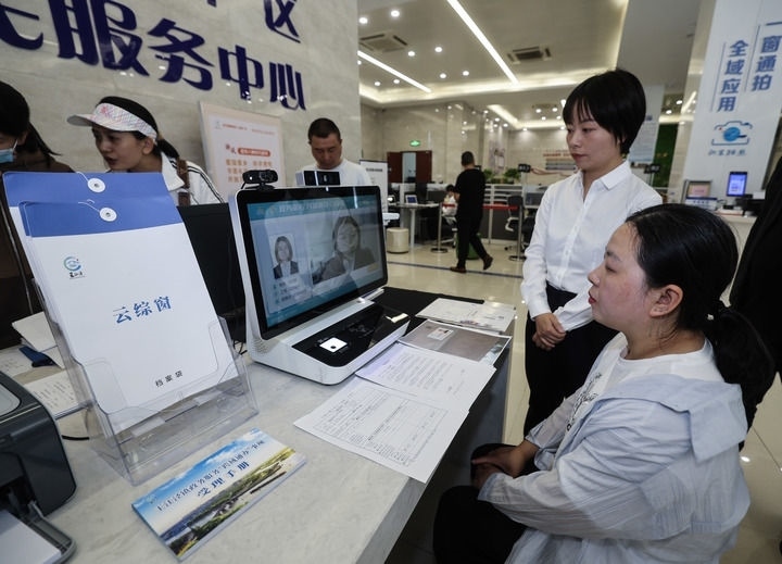 在浙江省嘉興市秀洲區(qū)王江涇鎮(zhèn)便民服務(wù)中心的“跨域通辦·云綜窗”窗口，辦理開(kāi)業(yè)登記的個(gè)體工商戶（右一）通過(guò)該系統(tǒng)與江蘇省蘇州市吳江區(qū)盛澤鎮(zhèn)行政審批局工作人員視頻連線，進(jìn)行身份讀取及材料線上審核（2024年5月9日攝）。新華社記者 徐昱 攝