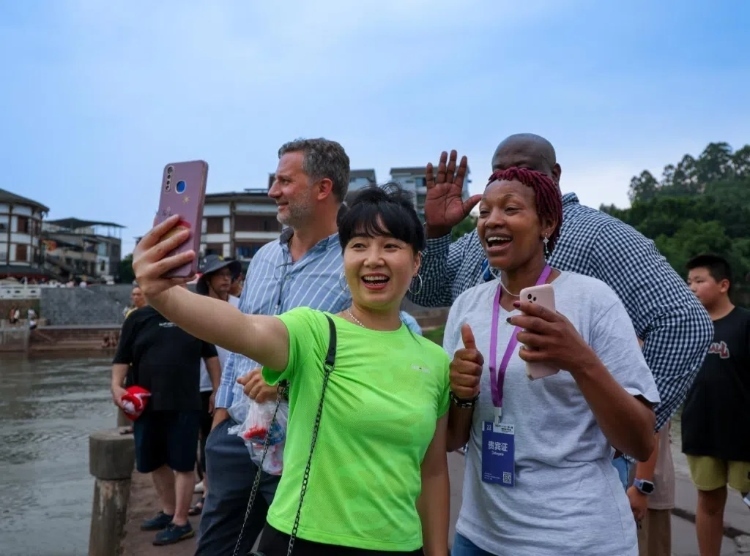 2024“一帶一路”媒體合作論壇聯(lián)合采訪調(diào)研行成員在樂山蘇稽古鎮(zhèn)與游客合影留念。本報(bào)記者 伊霄攝