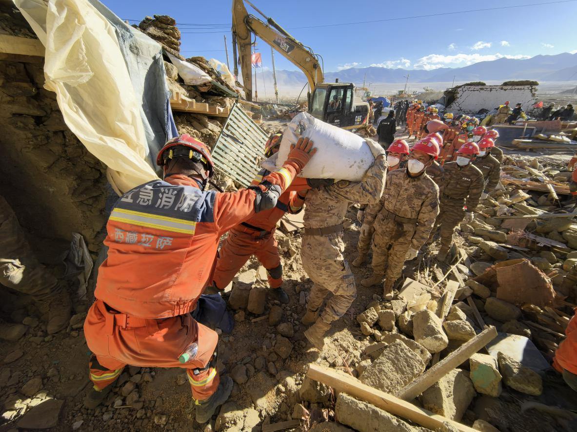 1月11日，定日縣長所鄉(xiāng)古榮村，應急消防等救援人員排隊接力搶運掩埋在倒塌房屋下的群眾財物。人民日報記者楊翹楚攝